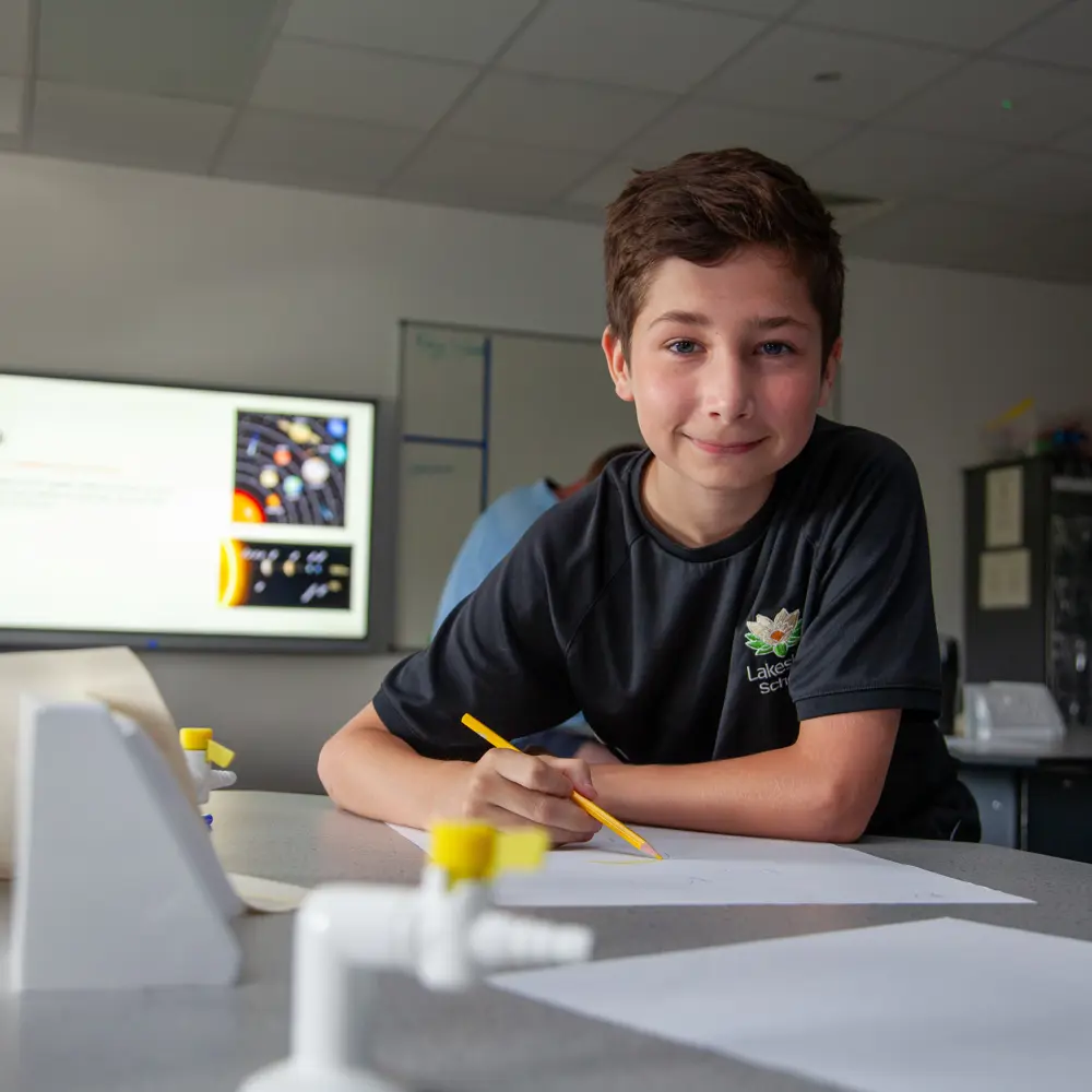 A young boy from Lakeside School working at a desk smiling at the camera