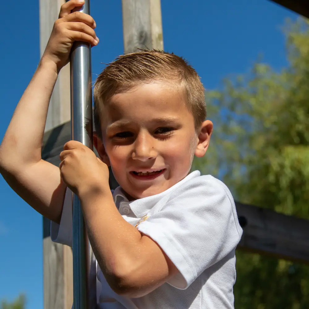 A young boy in a white polo shirt going down a fireman's pole in a playground