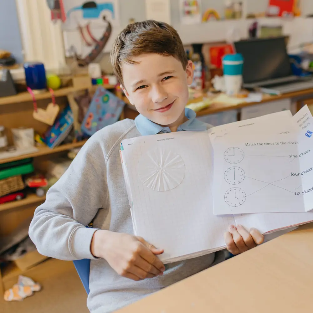 Young boy from Cedar House School sat at his desk showing off his class workbook