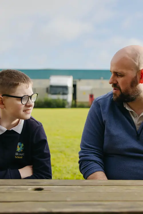 A young boy with glasses at Millcourt School sat on a bench with a member of staff