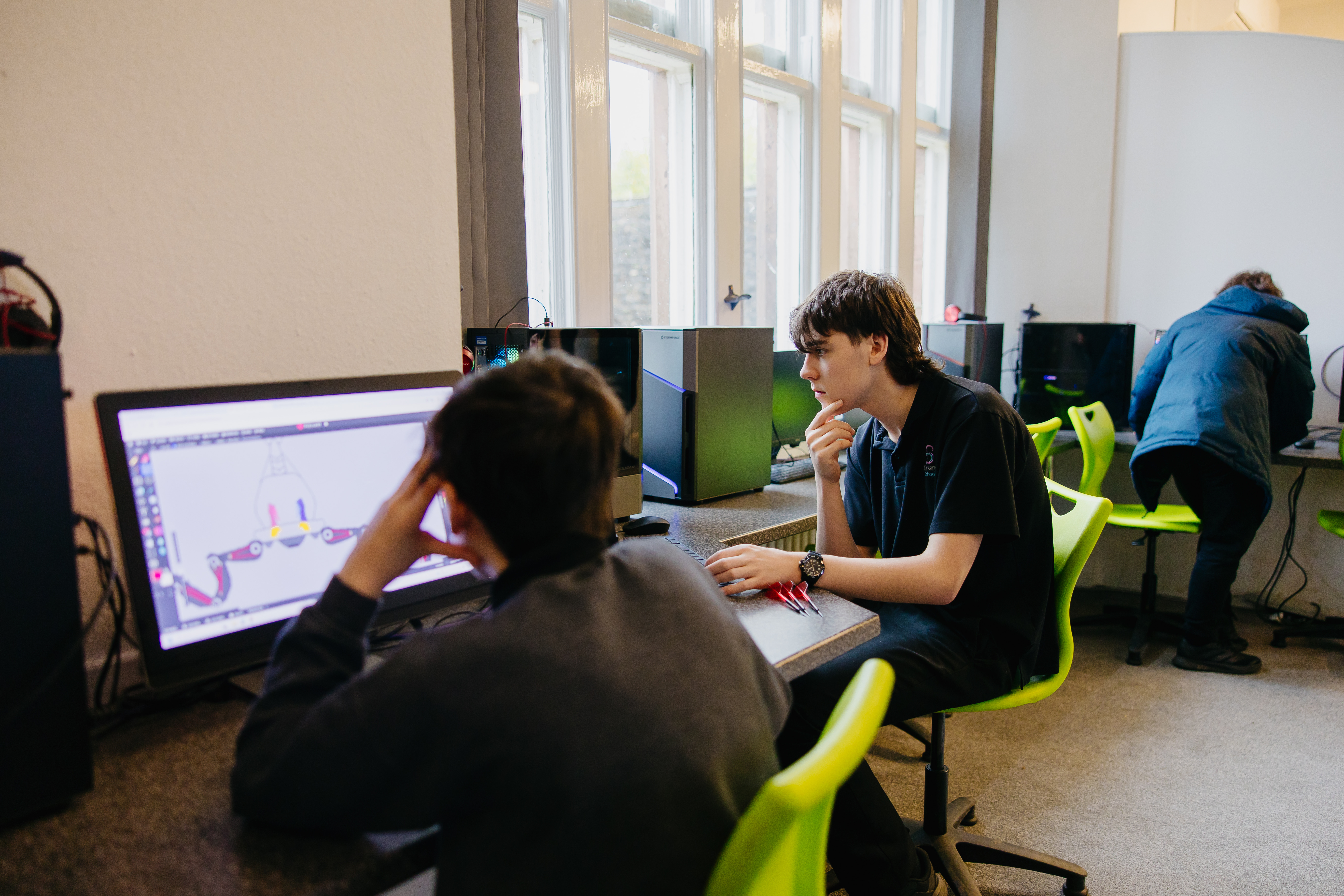 Students in a computer suite on green chairs looking a computers
