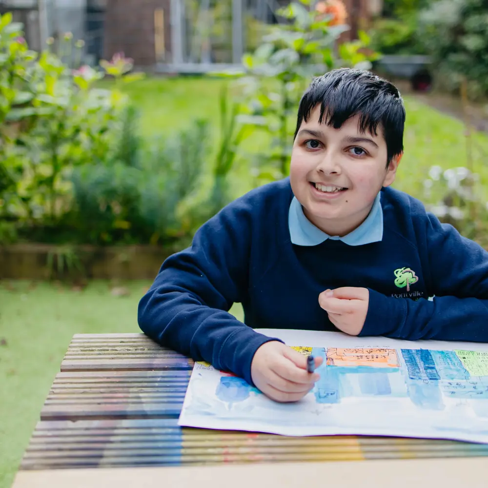 Young boy from Pontville School sat on a bench in the garden colouring