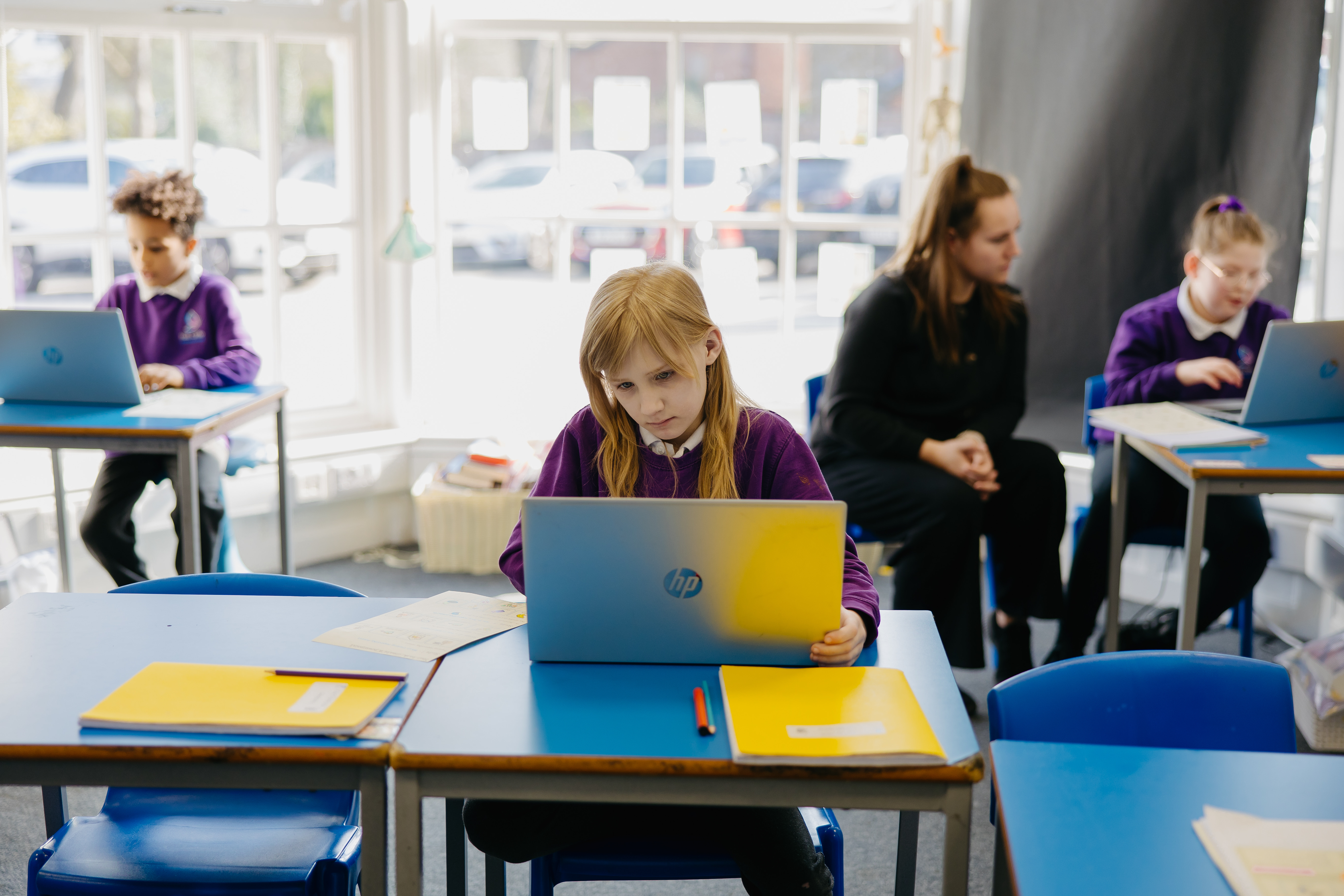 Three pupils learning in a classroom with laptops