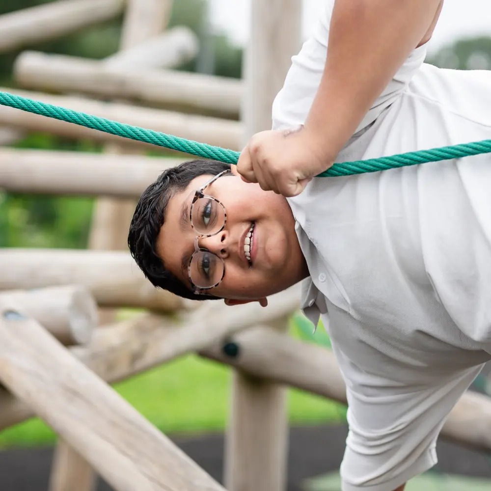 A young boy with glasses playing on the outdoor equipment at Luxborough Court School