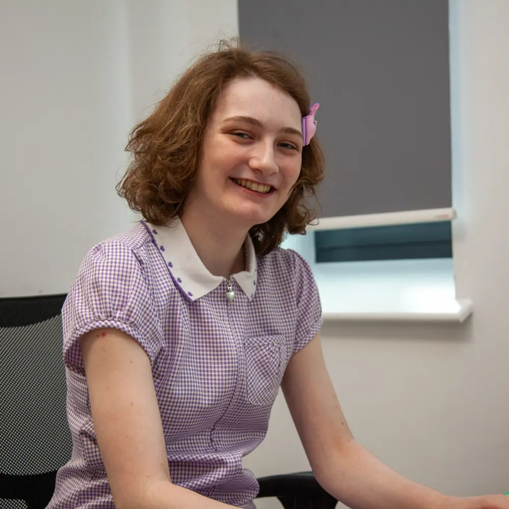 A young girl at Lakeside School wearing a checked purple and white dress smiling at the camera