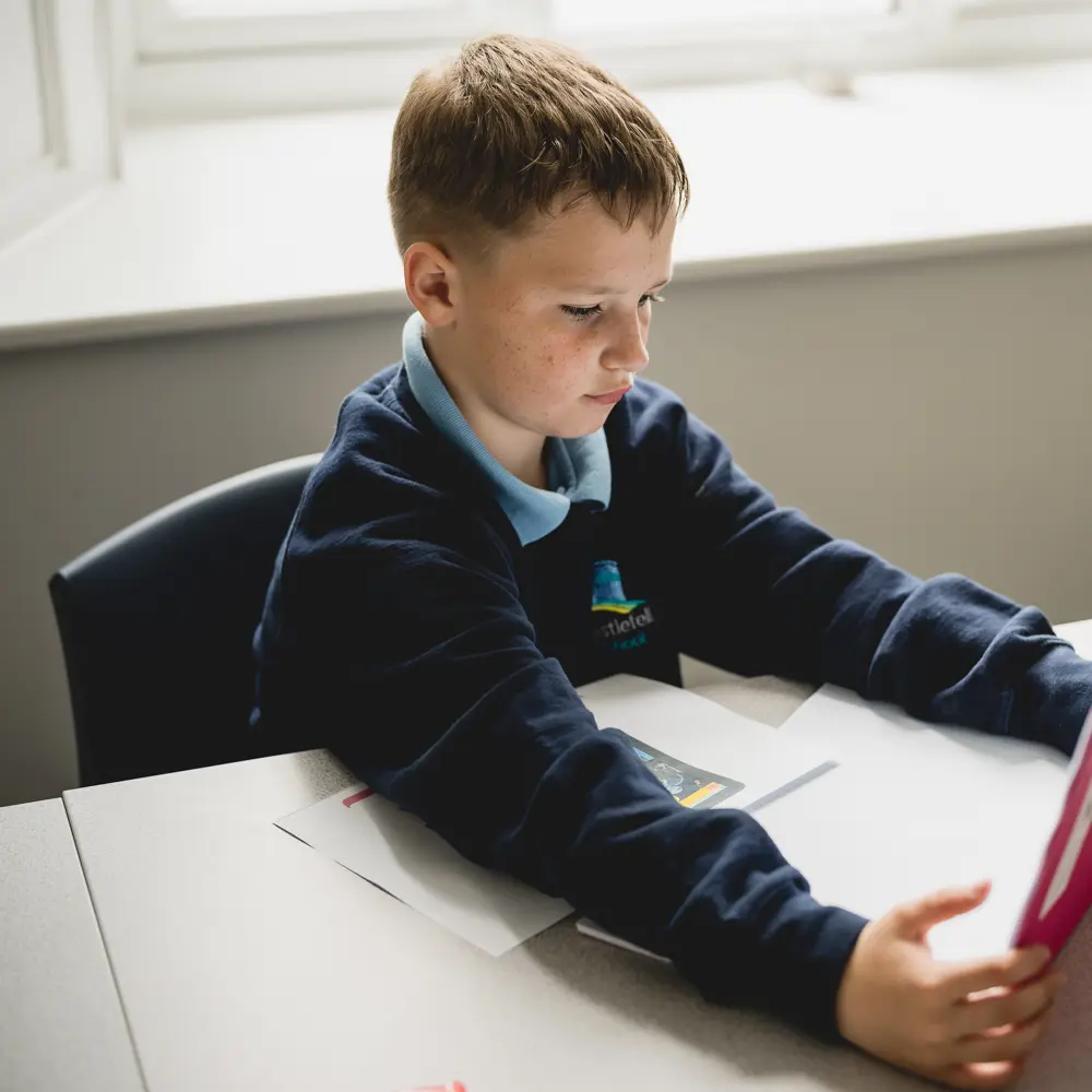 A young boy at Castlefell School sitting at a desk reading a book