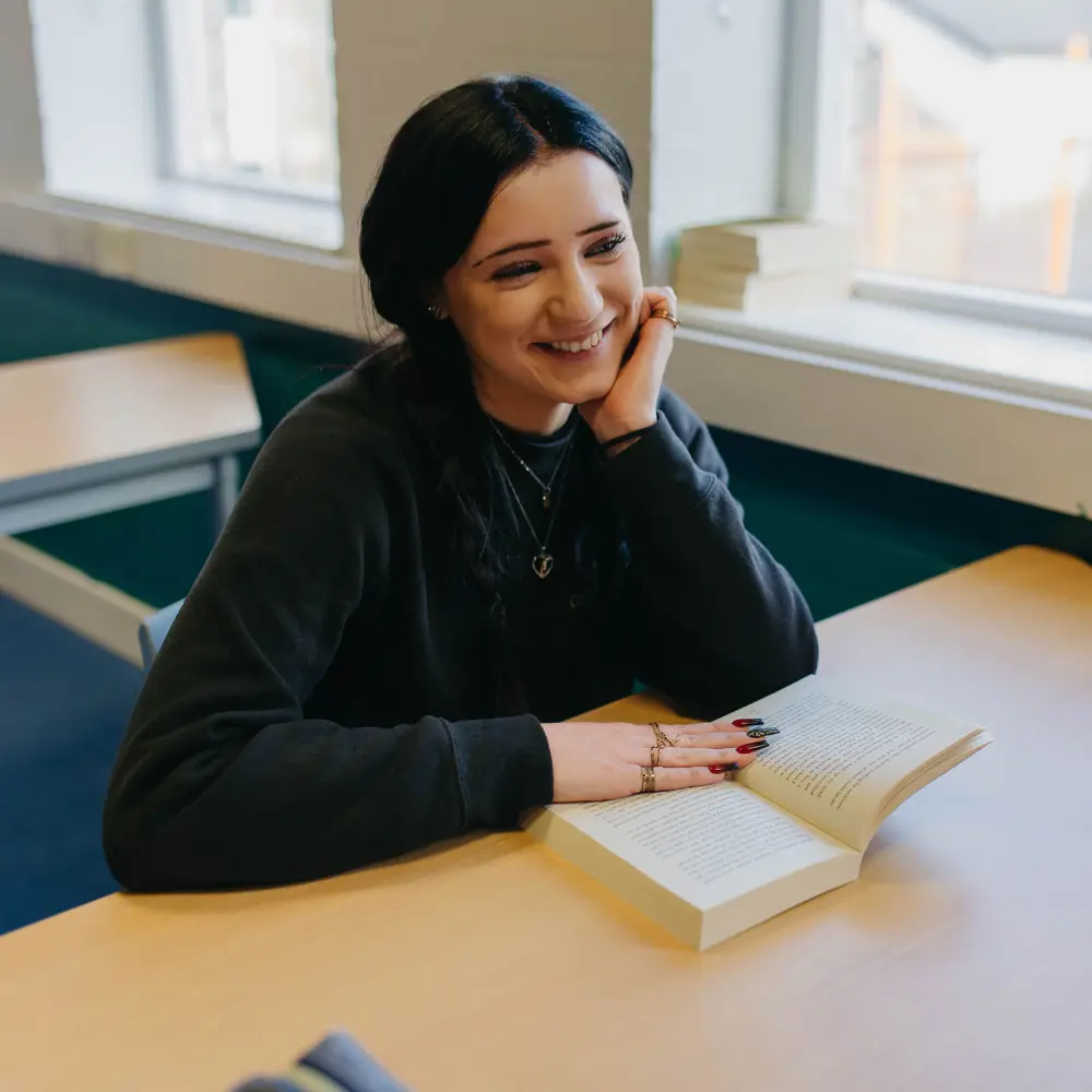 Girl from Cedar House School sat at a desk with her book reading