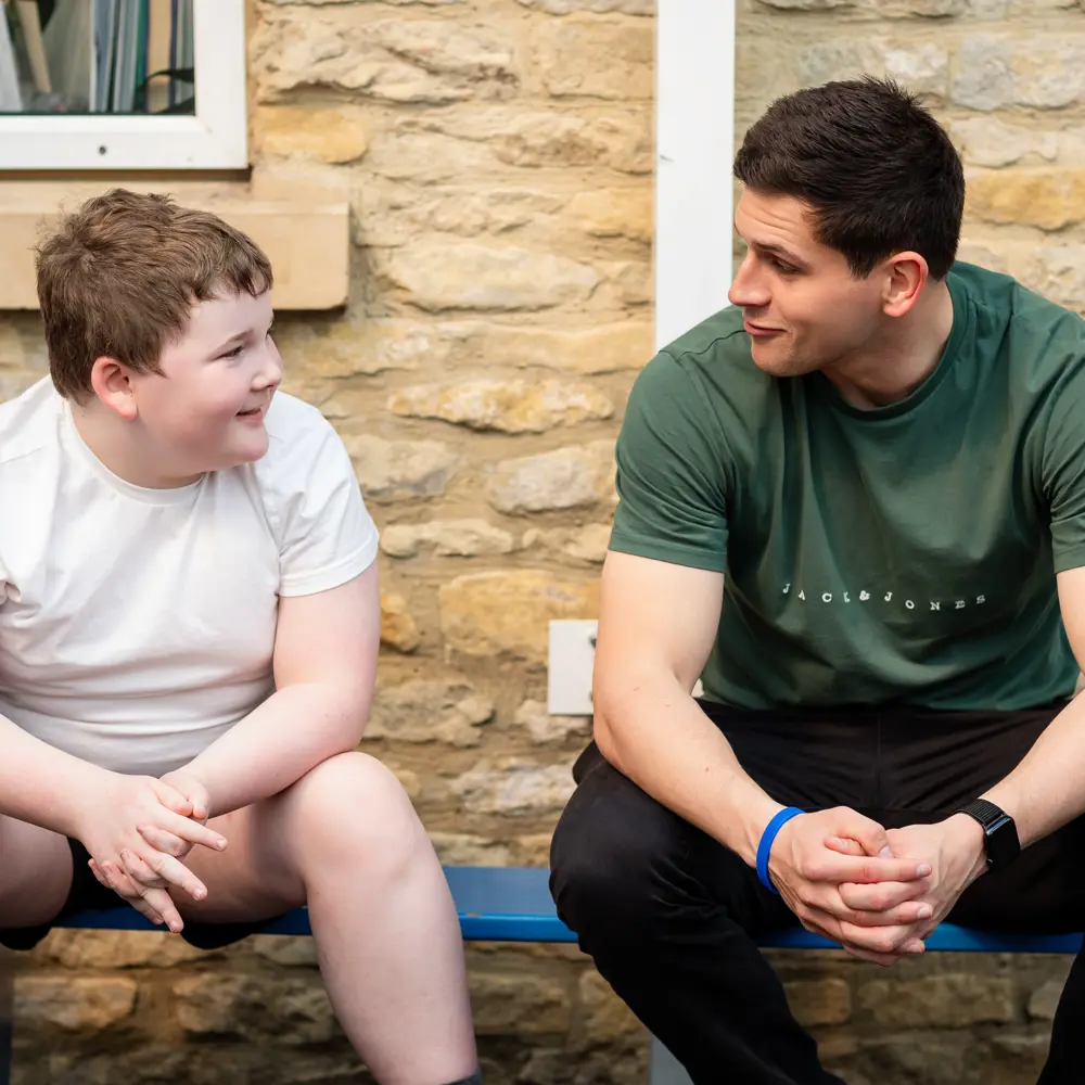 A young boy from Chilworth House School sat on a bench outside with a member of staff