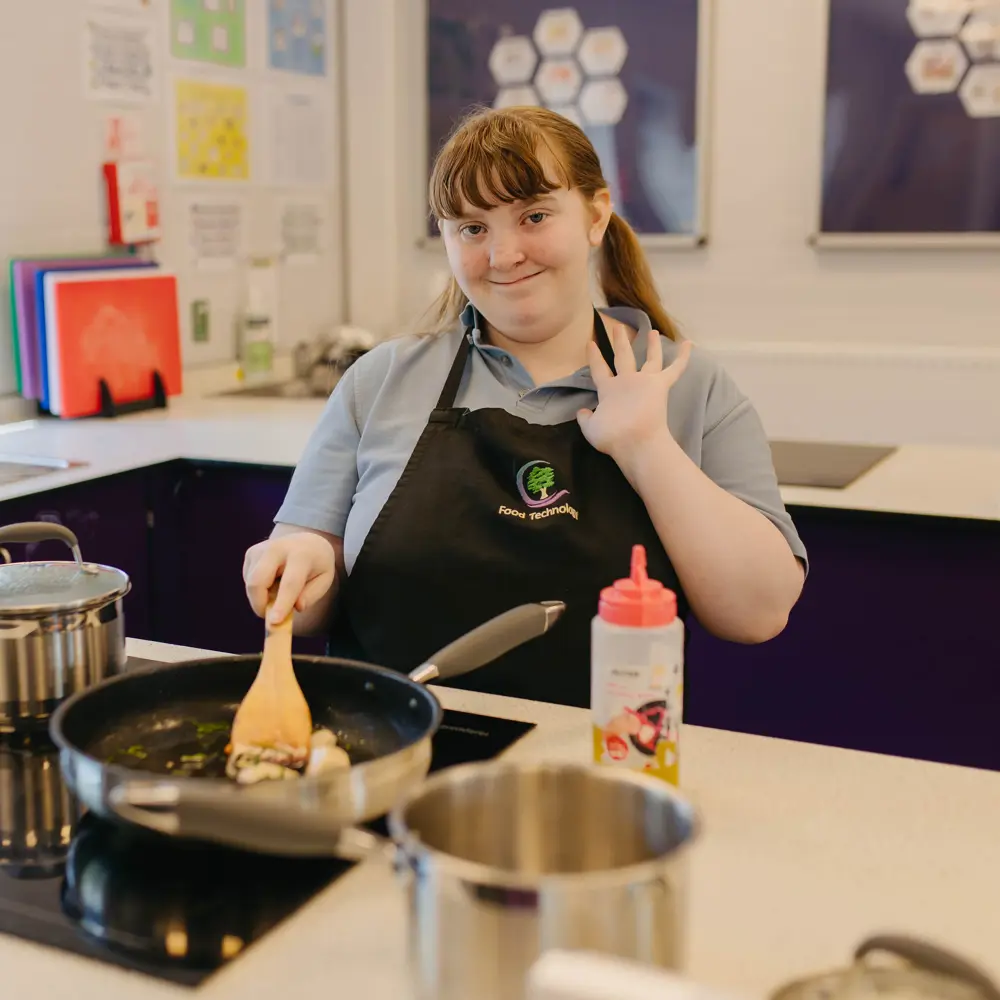 A young girl at Cedar House School waving at the camera whilst cooking