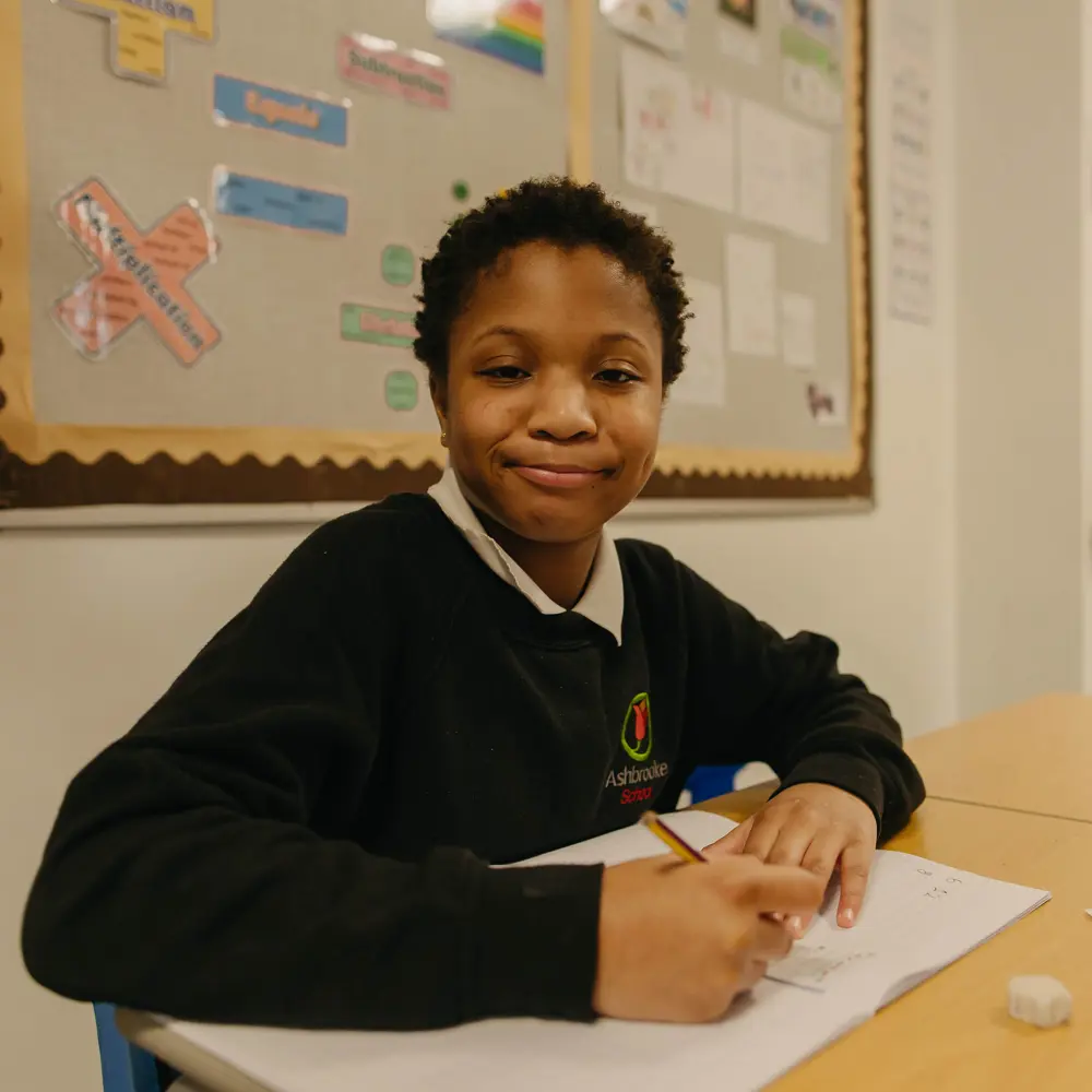 Young pupil smiling and completing classwork in a classroom at Ashbrooke School