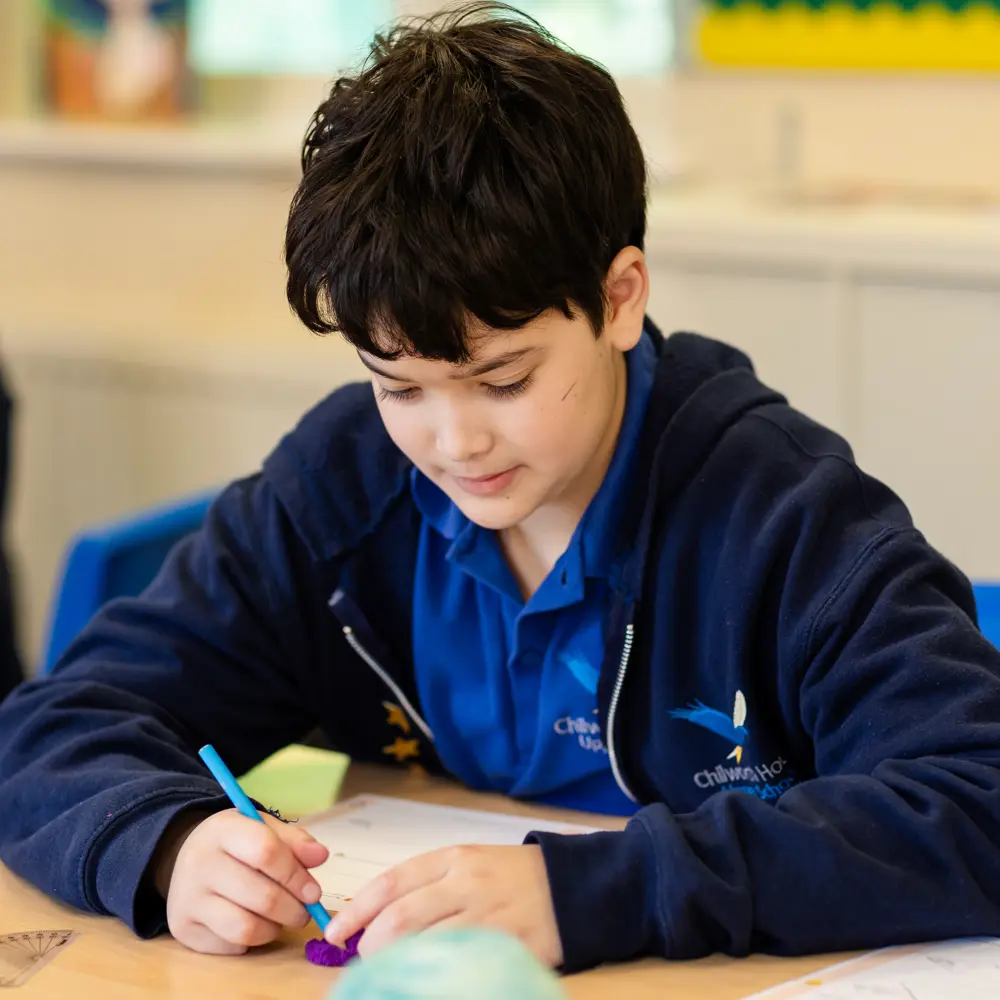 A young boy at Chilworth House Upper School working in the classroom wearing his school uniform